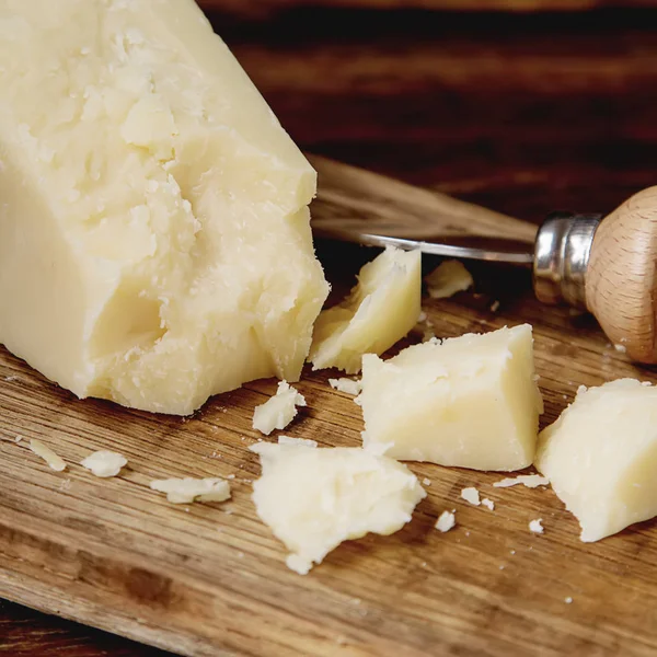 Pedaço de queijo parmesão italiano com uma faca. Backgro de madeira escura — Fotografia de Stock