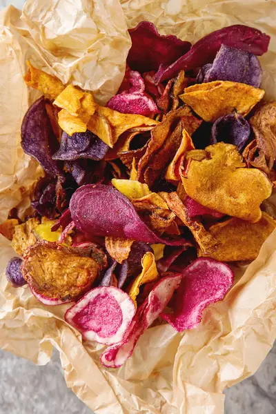 Beet and carrot salty chips on baking paper in an old brown wick — Stock Photo, Image