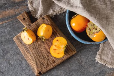 Bir ahşap tepsi üzerinde mavi bir kasede olgun turuncu Trabzon hurması. Diyet, veya 