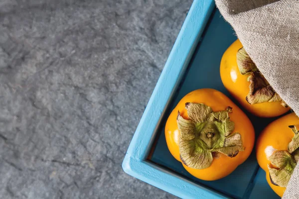 青い木製トレイに熟したオレンジ柿。食事療法、または概念 — ストック写真
