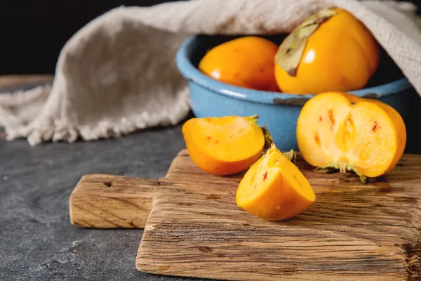 木製トレイ上に青いボウルに熟したオレンジ色の柿。ダイエット、または — ストック写真