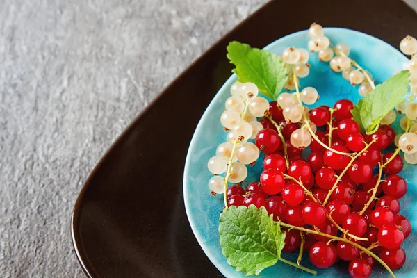 Red and white ripe currant on a blue plate. Dark wood background