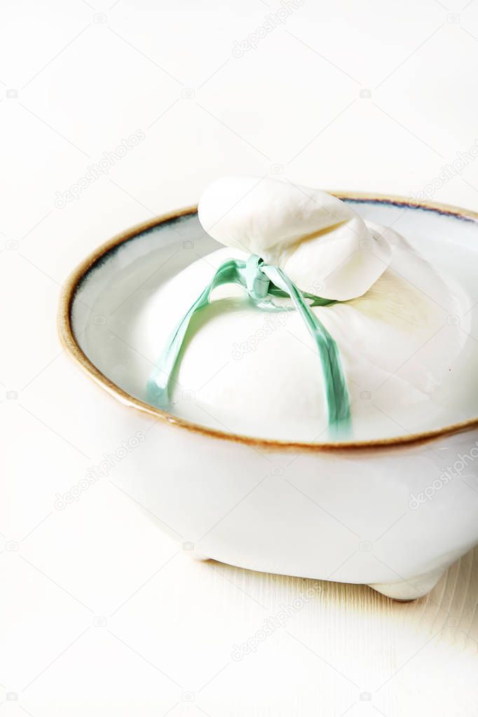 Italian fresh burrata cheese in a ceramic bowl. Light white back
