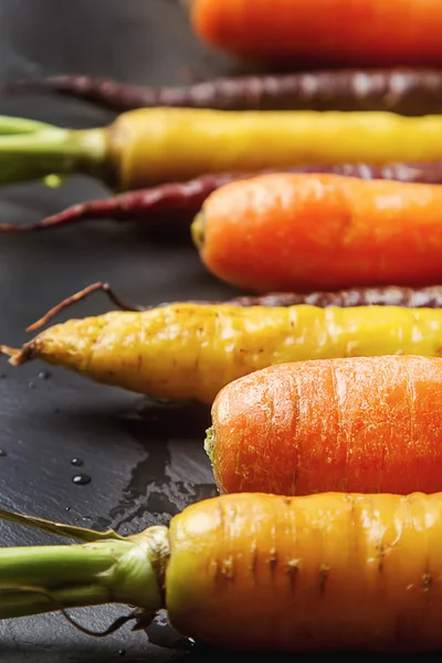 Carottes mûres noires, orange et jaunes. Fond en pierre sombre. A — Photo