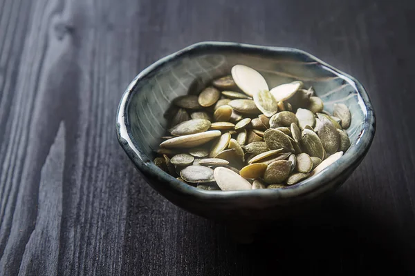 Pumpkin seeds in the blue plate. Black wood background. — Stock Photo, Image