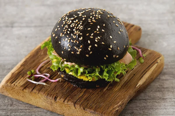 Black burger with salmon fish, lettuce, mustard. Light white bac