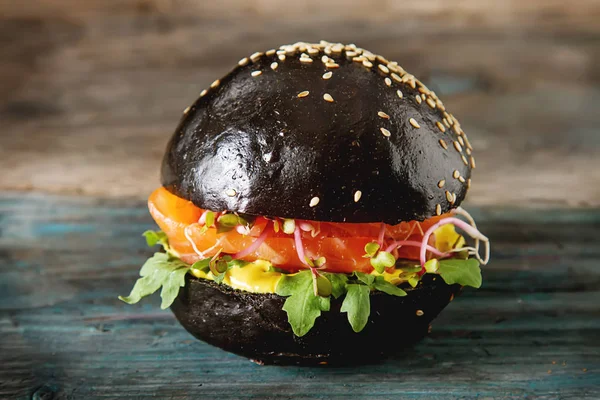 Black burger with salmon fish, lettuce, mustard. Dark background