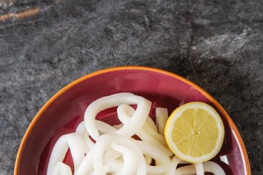 White seafood. Squid rings with lemon on a ceramic plate. Dark b clipart