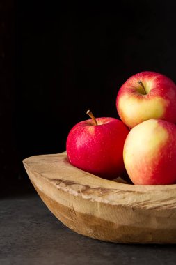 Ahşap bir kase içinde olgunlaşmış sulu elma. Koyu arka plan. Te için alan
