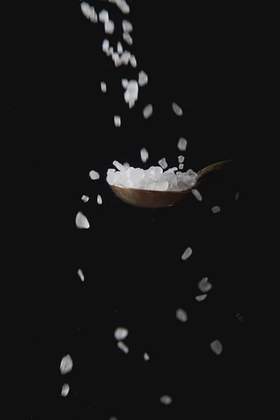 Cucchiaio di metallo con sale bianco, spezie che cadono. Fondo nero. s — Foto Stock