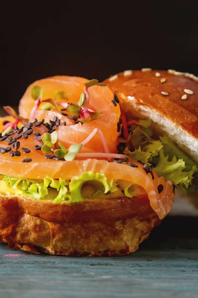 Burger with salmon fish, leaf salad, mustard. Dark wooden backgr