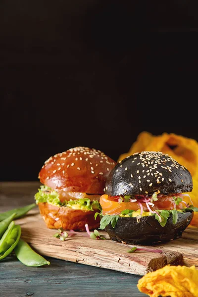 Black burger with salmon fish, lettuce, mustard. Dark background