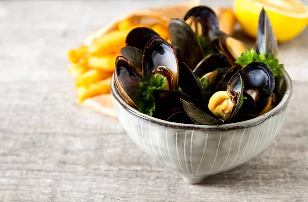 Mussels with herbs in a bowl with lemon and French fries on a wh — Stock Photo, Image