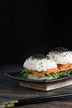 Somon füme, yeşil salata ve soya sosu ile pirinç suşi-hamburger. Modern sağlıklı gıda. Koyu arka plan