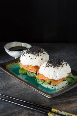 Somon füme, yeşil salata ve soya sosu ile pirinç suşi-hamburger. Modern sağlıklı gıda. Koyu arka plan