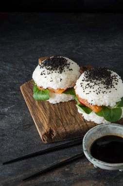 Somon füme, yeşil salata ve soya sosu ile pirinç suşi-hamburger. Modern sağlıklı gıda. Koyu arka plan