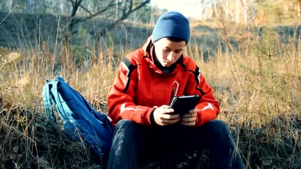 Хлопчик-підліток у використанні планшета в осінньому лісі — стокове відео