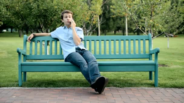 Adolescente sentado no banco falando o telefone celular — Vídeo de Stock