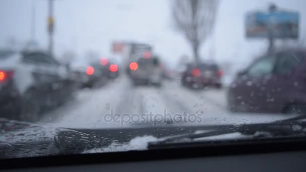 Vista a través del parabrisas en la escena desenfocada en la carretera nevada de la ciudad — Vídeo de stock