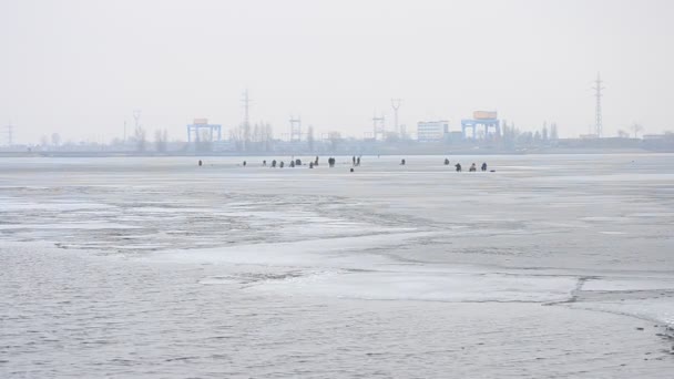 Зимние рыболовы на льду бассейна для хранения замороженной воды на фоне гидроэлектростанции — стоковое видео