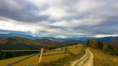 Sonbahar. Toprak yol, orman, renkli ağaçlar, hızlı kabarık bulutlar ve gölgeler ile fantastik dağ manzarası. Timelapse.
