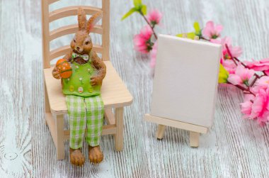 Bir yumurta, resim şövale ve çiçekler ile dışkı ahşap arka plan üzerinde oturan Paskalya tavşanı