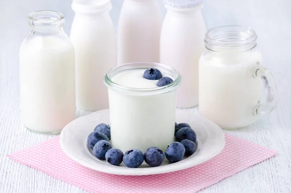 Una tazza di yogurt con mirtilli e diverse bottiglie di bevanda yogurt e latte sul tavolo — Foto Stock