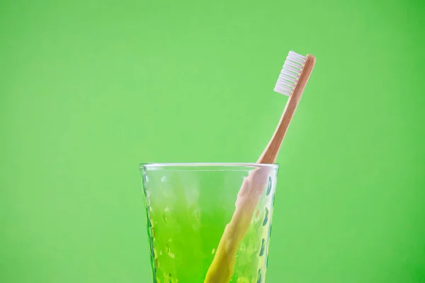 Альтернативная деревянная зубная щетка в стакане на зеленом фоне, горизонтальная — стоковое фото