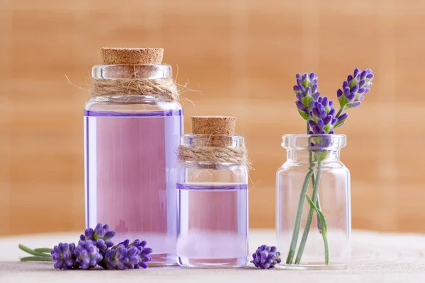 Лавандовая вода и масло в стеклянных бутылках и свежие цветы лаванды на пне и коричневом фоне — стоковое фото