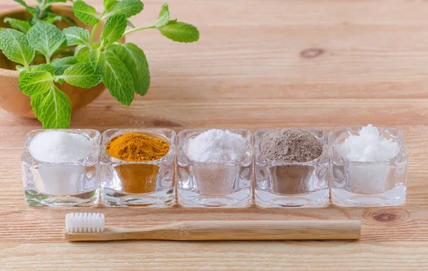 Alternative natural toothpaste xylitol or soda, turmeric - curcuma, himalayan salt, clay or ash, coconut oil and wood toothbrush, mint on wooden — Stock Photo, Image
