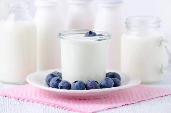 Een kopje yoghurt met blueberrys en verschillende flesjes drinken van yoghurt en melk op tafel — Stockfoto