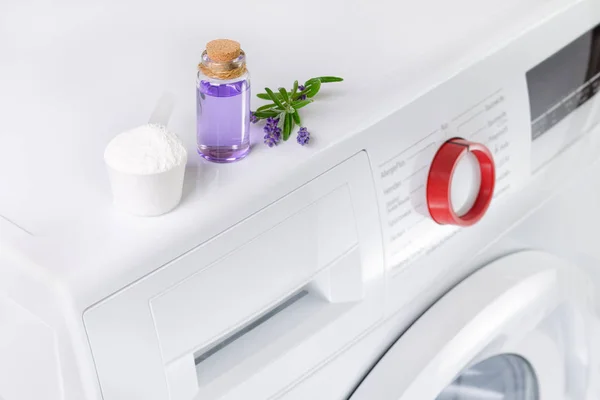 Натуральный стиральный порошок с эфирным маслом и лавандовыми цветами над стиральной машиной — стоковое фото