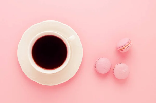 Rózsaszín macaroons házi és egy csésze kávét a rózsaszín háttér tónusú, felülnézet — Stock Fotó