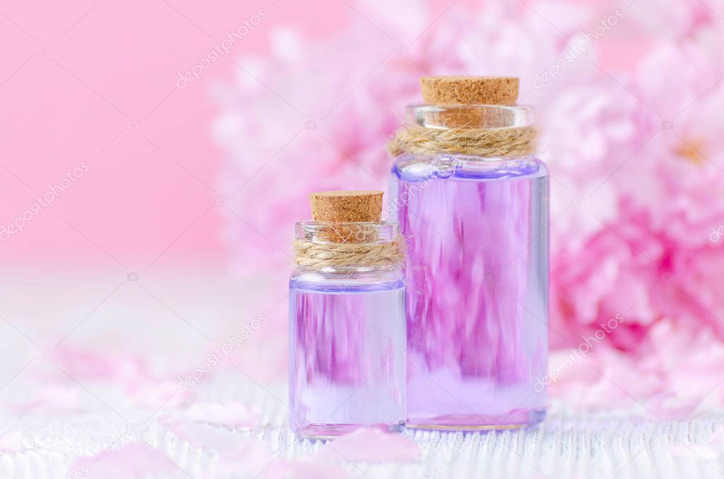 beautiful spa composition with two bottles of essential oils, fresh flowers on pink background, selective focus