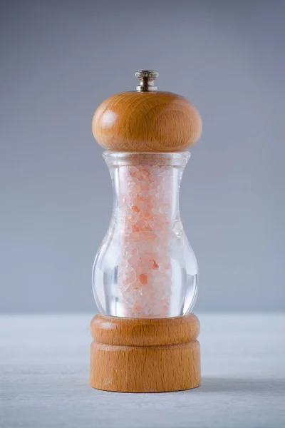 Růžová himálajská sůl krystaly v sklo dřevěný mlýnek na šedé — Stock fotografie