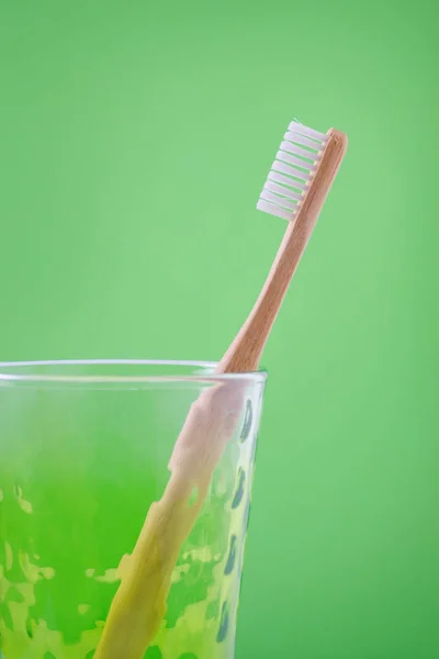 Альтернативная деревянная зубная щетка в стакане на зеленом фоне, вертикальная — стоковое фото