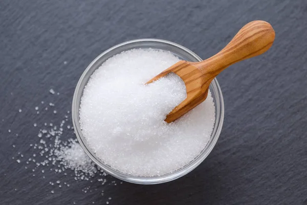 Xylitol or birch sugar in a wooden scoop and glass bowl on black background, selective focus — Stock Photo, Image