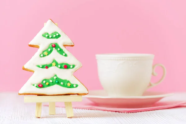 Christmas tree gingerbread on the painting easel with coffe cup on pink background, toned — Stock Photo, Image