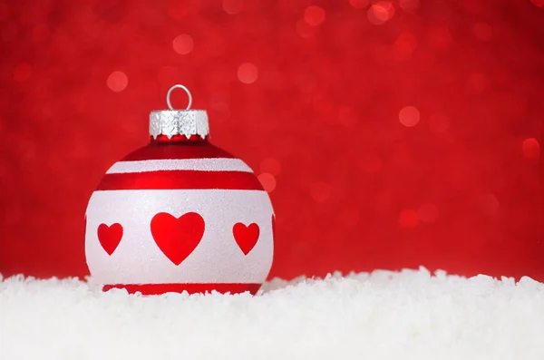 Christmas ball with heart in snow on red background with bokeh, selective focus and copy space Stock Photo