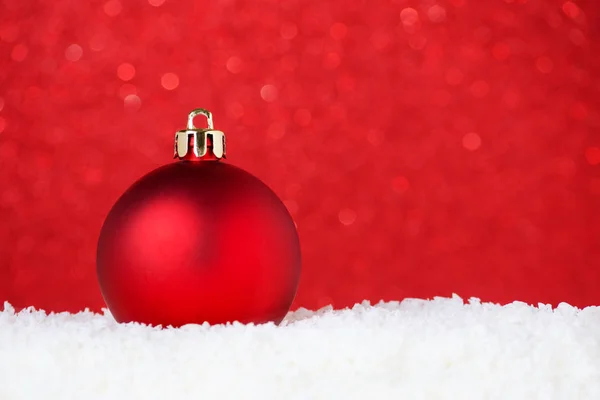 Christmas red bauble in snow on red background with bokeh, selective focus and copy space — Stock Photo, Image