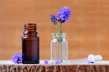 Lavanta esansiyel yağı kahverengi cam şişe ve doğal zemin üzerine taze lavanta çiçekleri