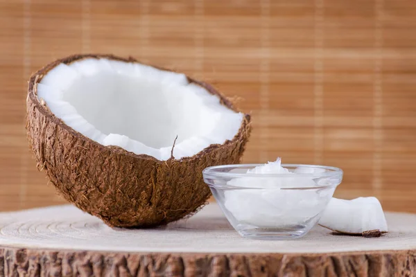 Óleo de coco orgânico em uma tigela de vidro e coco sobre fundo marrom natural — Fotografia de Stock