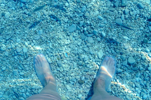 under water view of feet and water shoes, fish and pebble