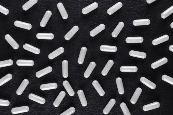Witte medicijncapsules op zwarte achtergrond, uitzicht van bovenaf — Stockfoto