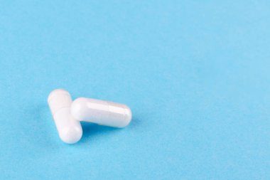 two white capsules of nutritional supplement on blue background with copy space