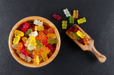 Ahşap bir kasede renkli jöle şekerler ve siyah arka planda kepçe, yukarıdan görünüm