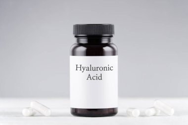Gri üzerine besin takviyesi hyaluronic asit şişesi ve kapsüller
