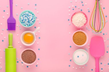 fırın malzemeleri, yumurta, un, kakao, şeker, tatlı dekorasyon ve mutfak aletleri pembe arka planda
