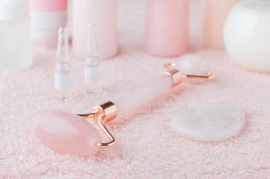 Spa ve sağlık ürünlerinin güzel bileşimi, yüz gülü kuvars silindiri ve pastel pembe arka planda yüz serumu, seçici odaklanma