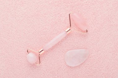 Gerçek gül kuvars yüz silindiri ve gua sha taşı pastel pembe arka planda, düz yatıyordu